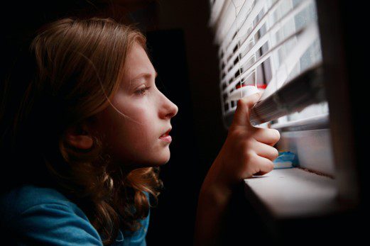 A girl in a dark room looks out a window