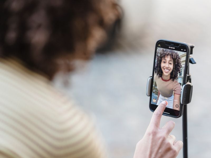 A woman recording a video on her cell phone on a tripod.