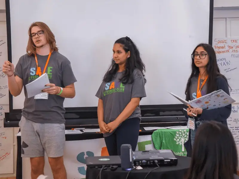 Three members of the SAVE Promise Club presenting in a conference room.