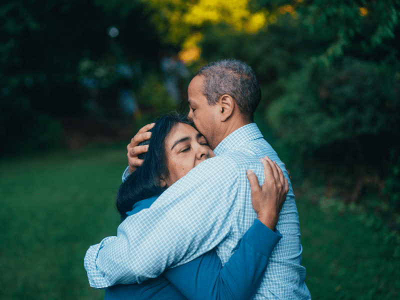 A man and woman hugging one another somberly.