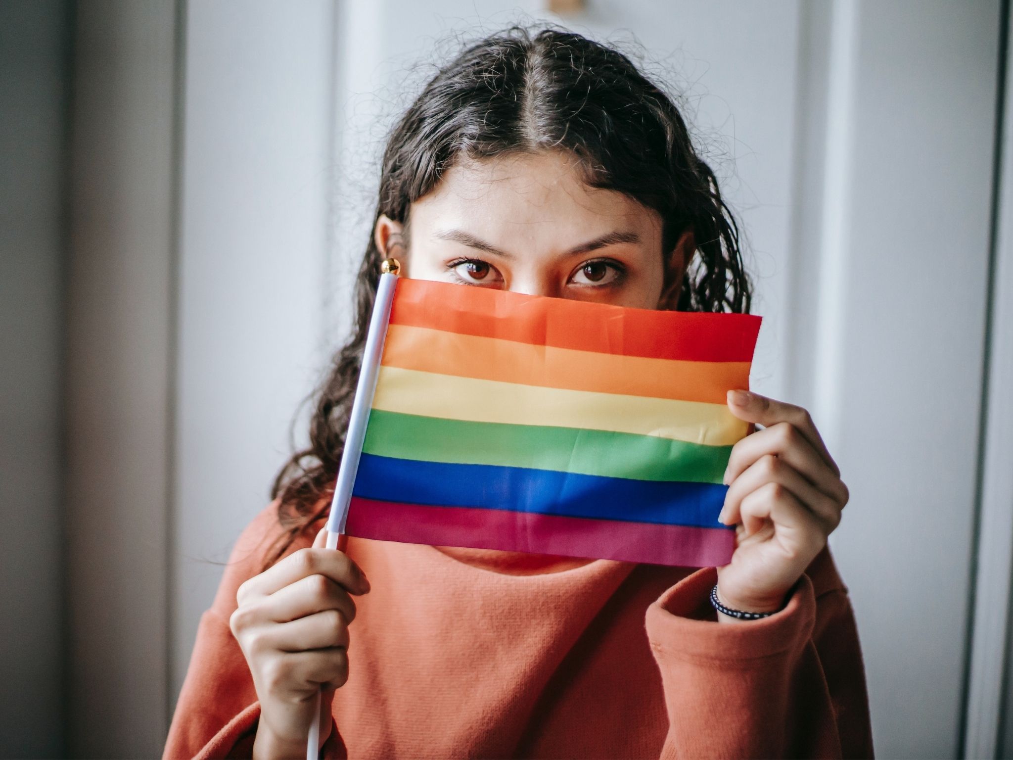 Young woman looking at the camera, holding a pride flag which obscures the rest of her face.
