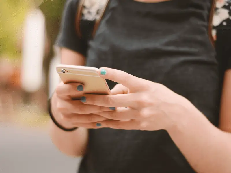 A woman with blue nails is holding a cell phone and texting