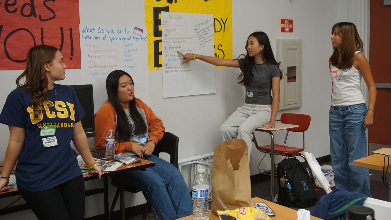Student pointing at a poster in a classroom while peers interact